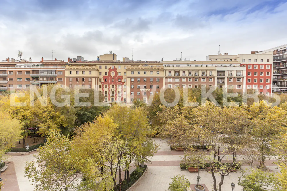 Cityscape view of a park with yellow trees in front of apartment buildings under a cloudy sky.