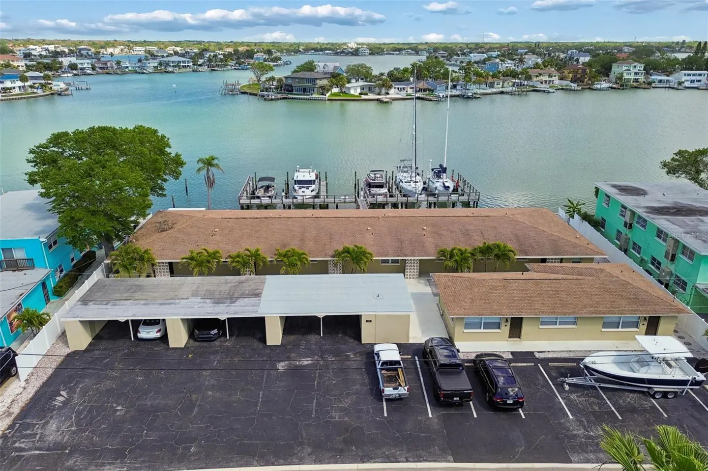 Aerial view of a tan apartment building with boat docks on a waterway. Cars are parked in the lot.