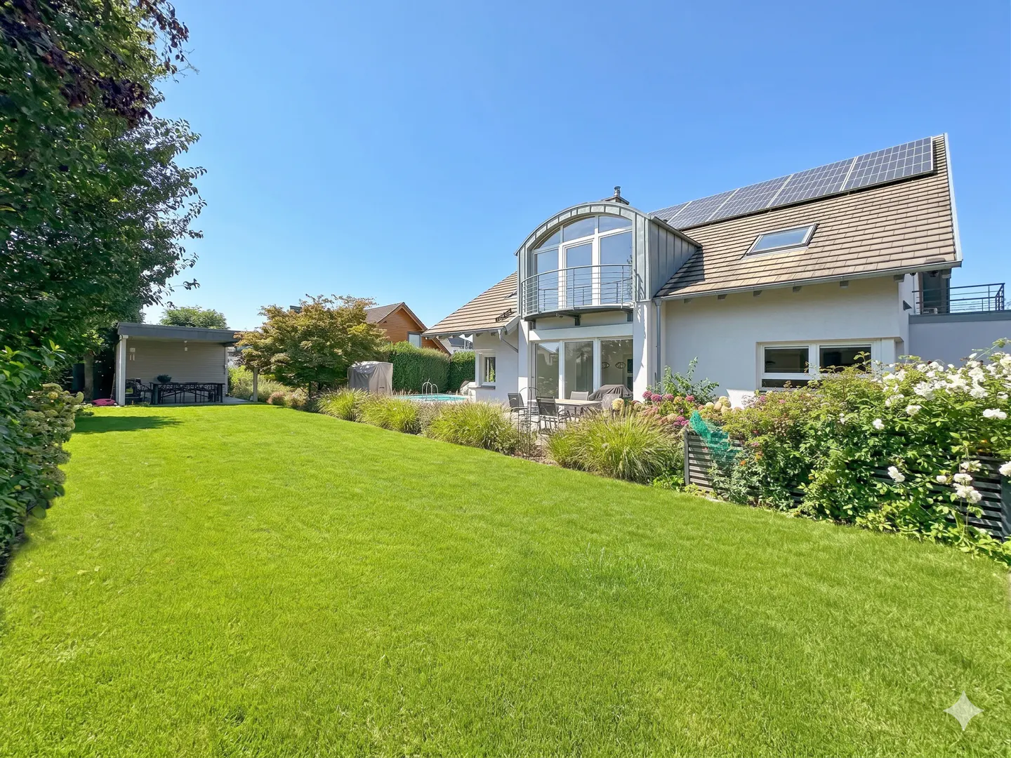 A white house with a green lawn, patio, and solar panels under a blue sky.