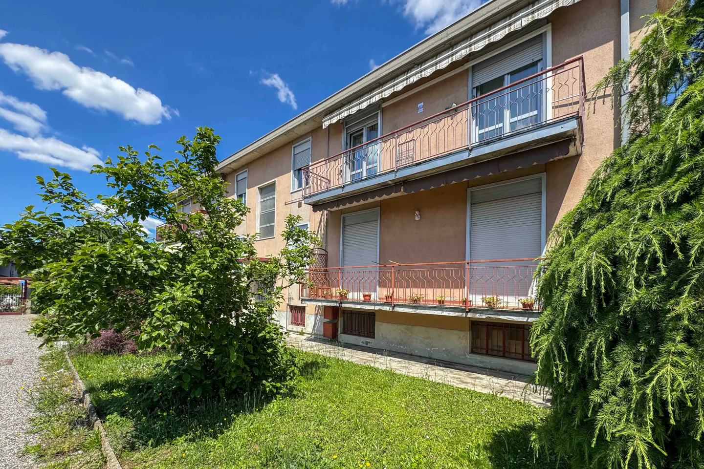 Exterior view of a peach-colored apartment building with two balconies, metal railings, and closed shutters under a blue sky.