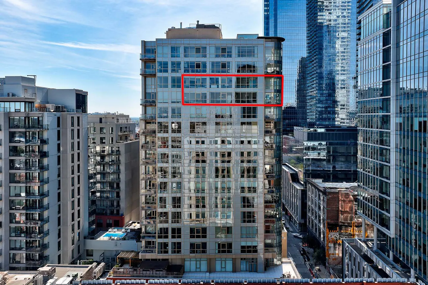 Exterior view of a modern high-rise building with a red rectangle highlighting a specific unit. Other buildings and a blue sky are in the background.