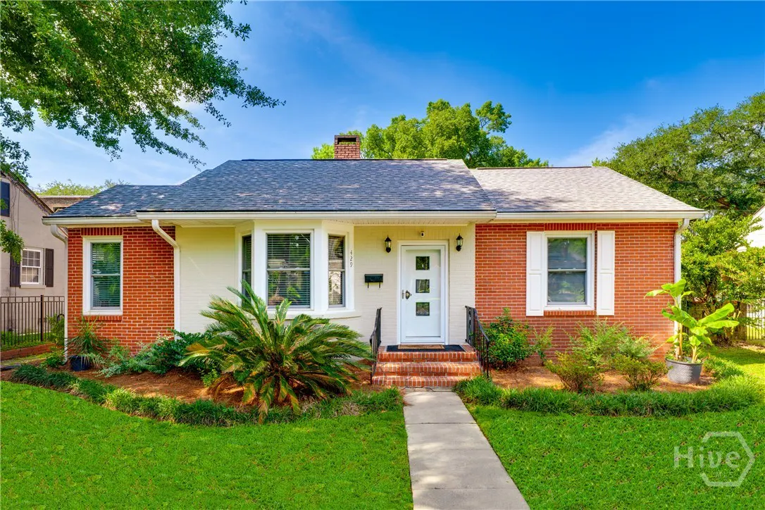Single-story brick house with a white front door, bay window, and green lawn under a clear blue sky.