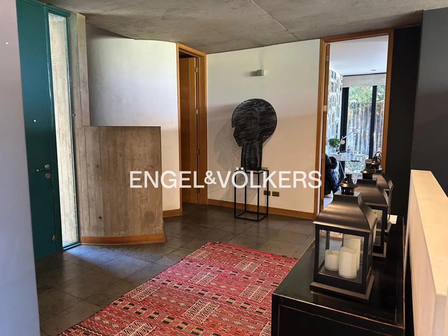 A home's foyer with a red patterned rug, a black head sculpture on a stand, and black lanterns on a black console table.