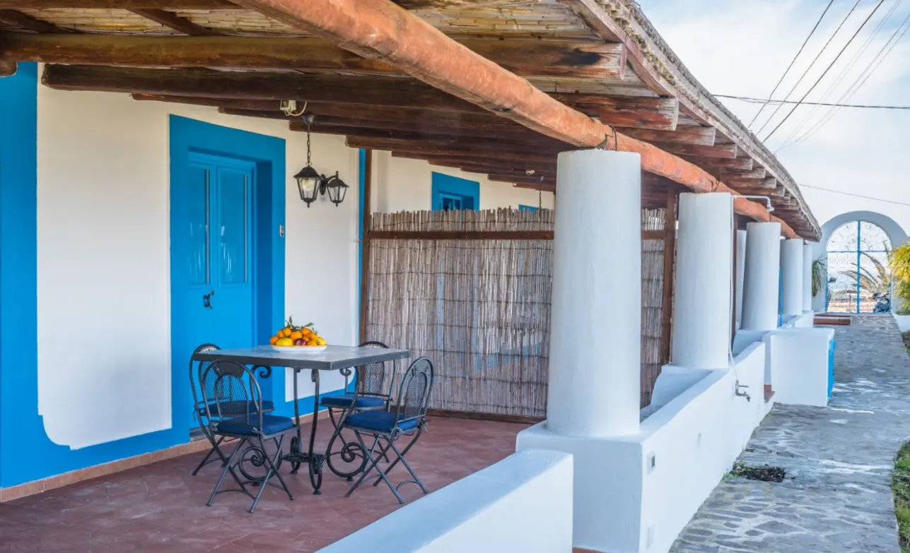 A patio with a dining table and chairs, featuring white walls, blue door frames, and a wooden pergola roof.