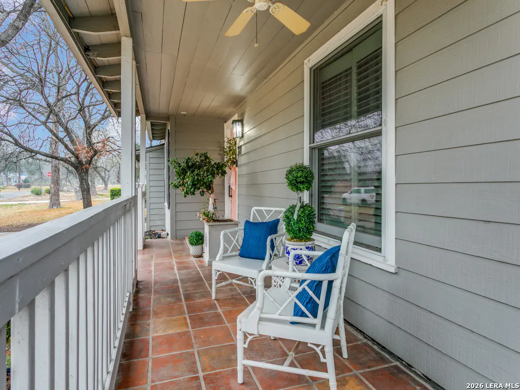Covered porch with white chairs, blue cushions, and potted plants. The floor is red tile and the house is gray siding.