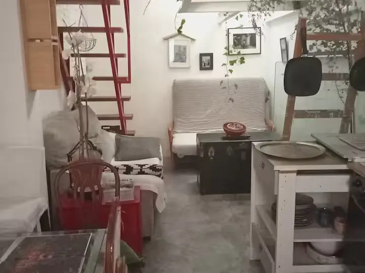 Small apartment interior with a red staircase, a sofa with a white cover, a dark coffee table, and a white kitchen island.