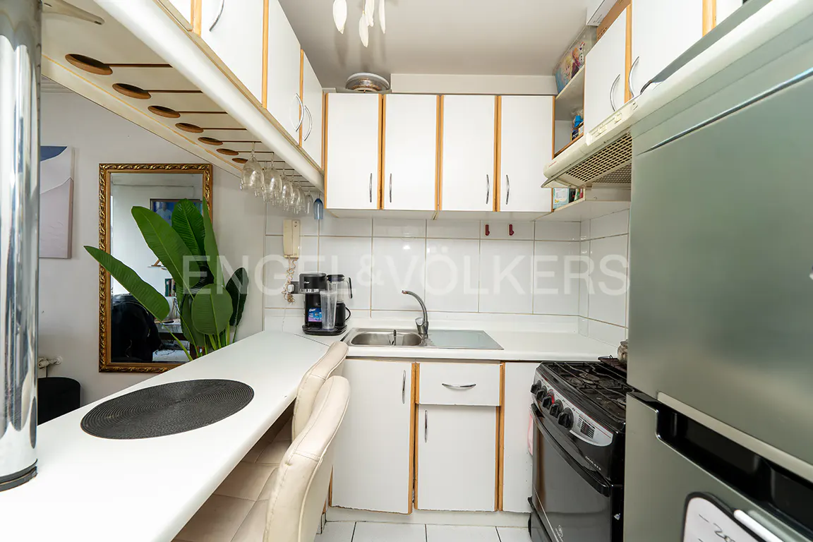 A compact kitchen with white cabinets, a breakfast bar, and stainless steel appliances. Wine glasses hang above the bar.
