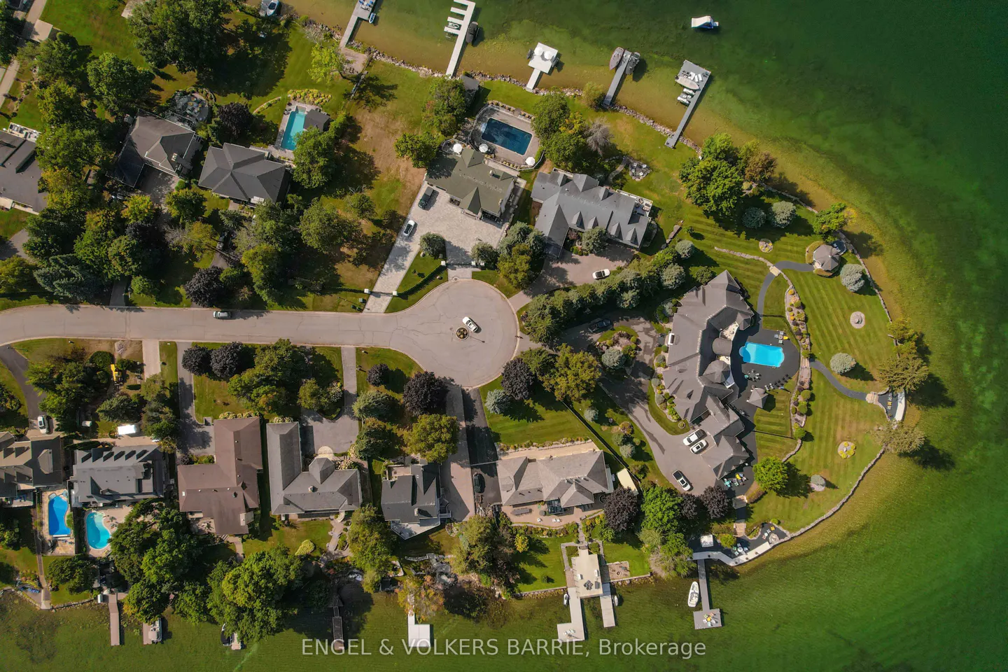 Aerial view of luxury homes on a green peninsula surrounded by water, some with pools and docks.