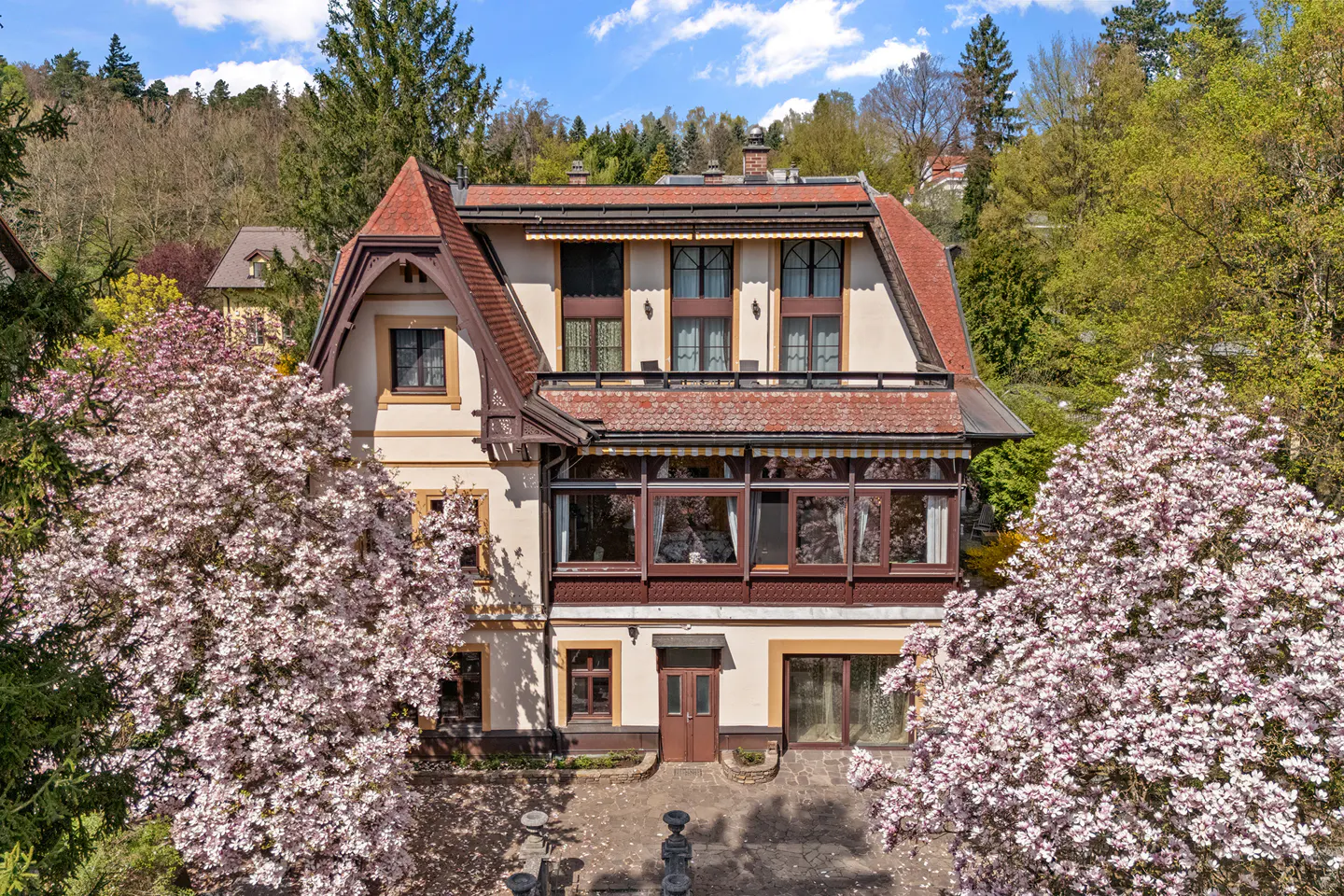 Exterior view of a three-story house with a red roof, surrounded by trees and pink magnolia blossoms.