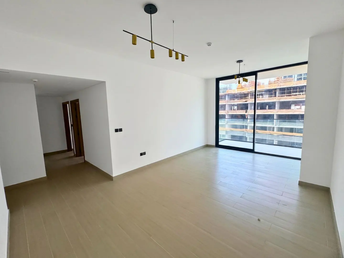 An empty, bright room with wood floors, white walls, and a large window with a view of a building under construction.