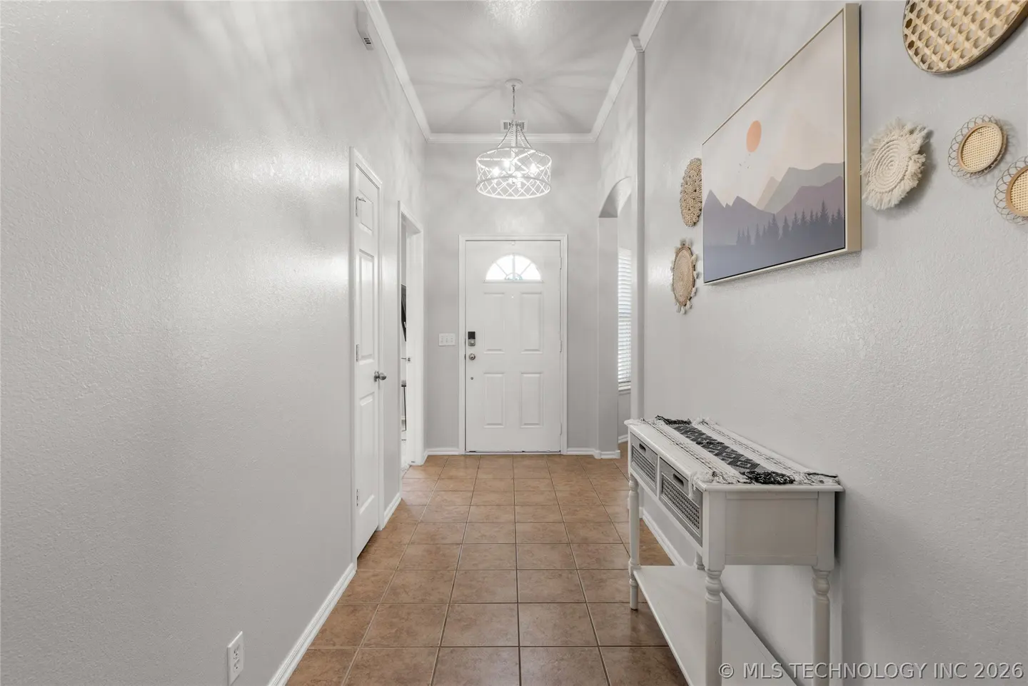 Bright entryway with tile floors, white walls, a modern chandelier, a white console table, and wall art decor.