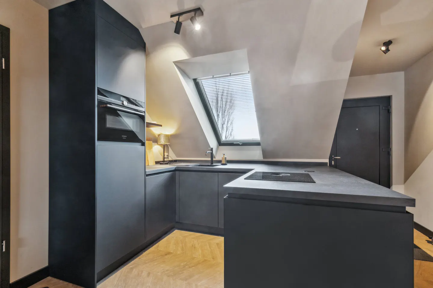 A modern kitchen with dark gray cabinets, a skylight, and herringbone wood floors.