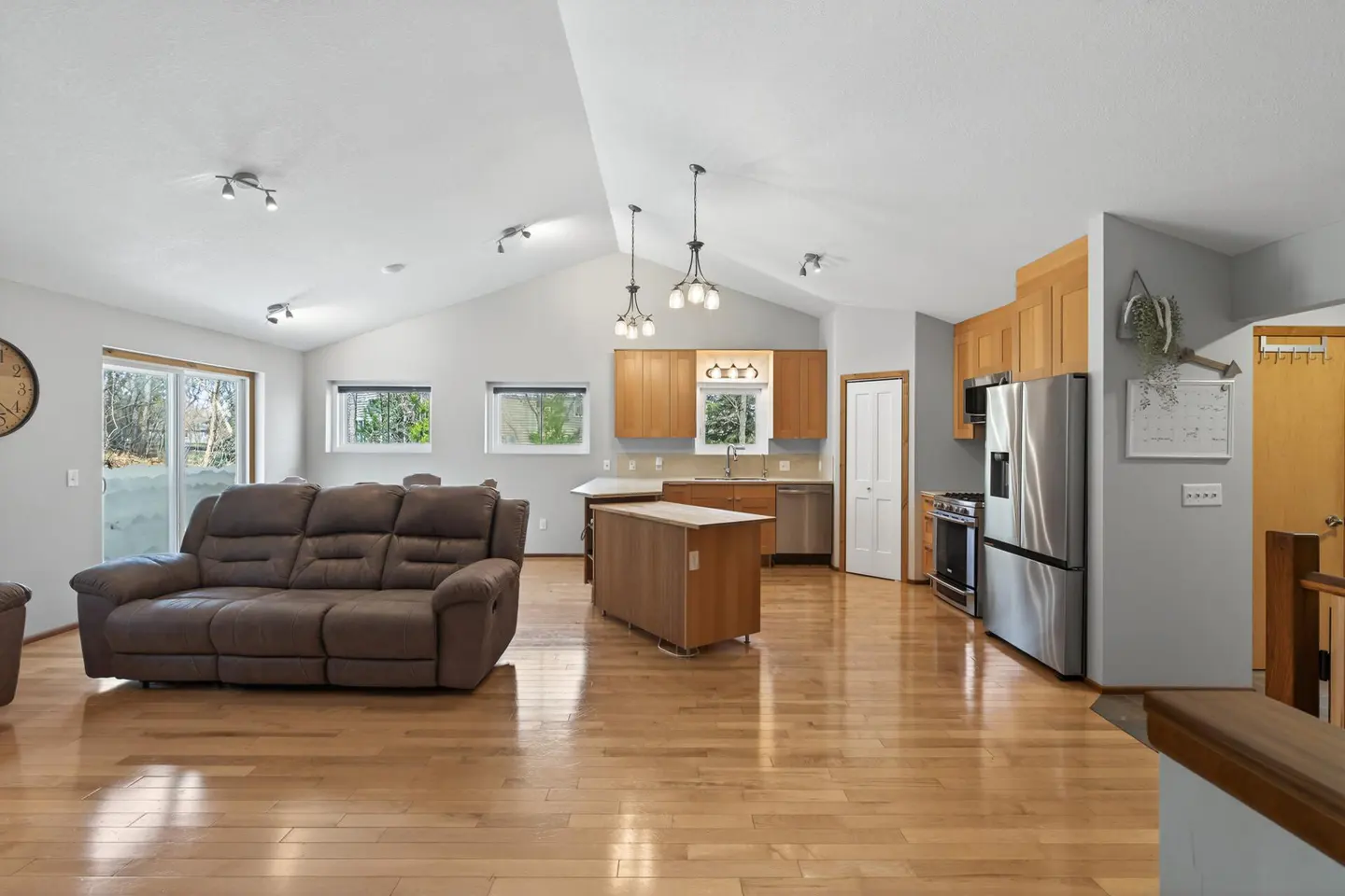 Open-concept living space with a brown leather sofa, wood floors, and a kitchen with stainless steel appliances.