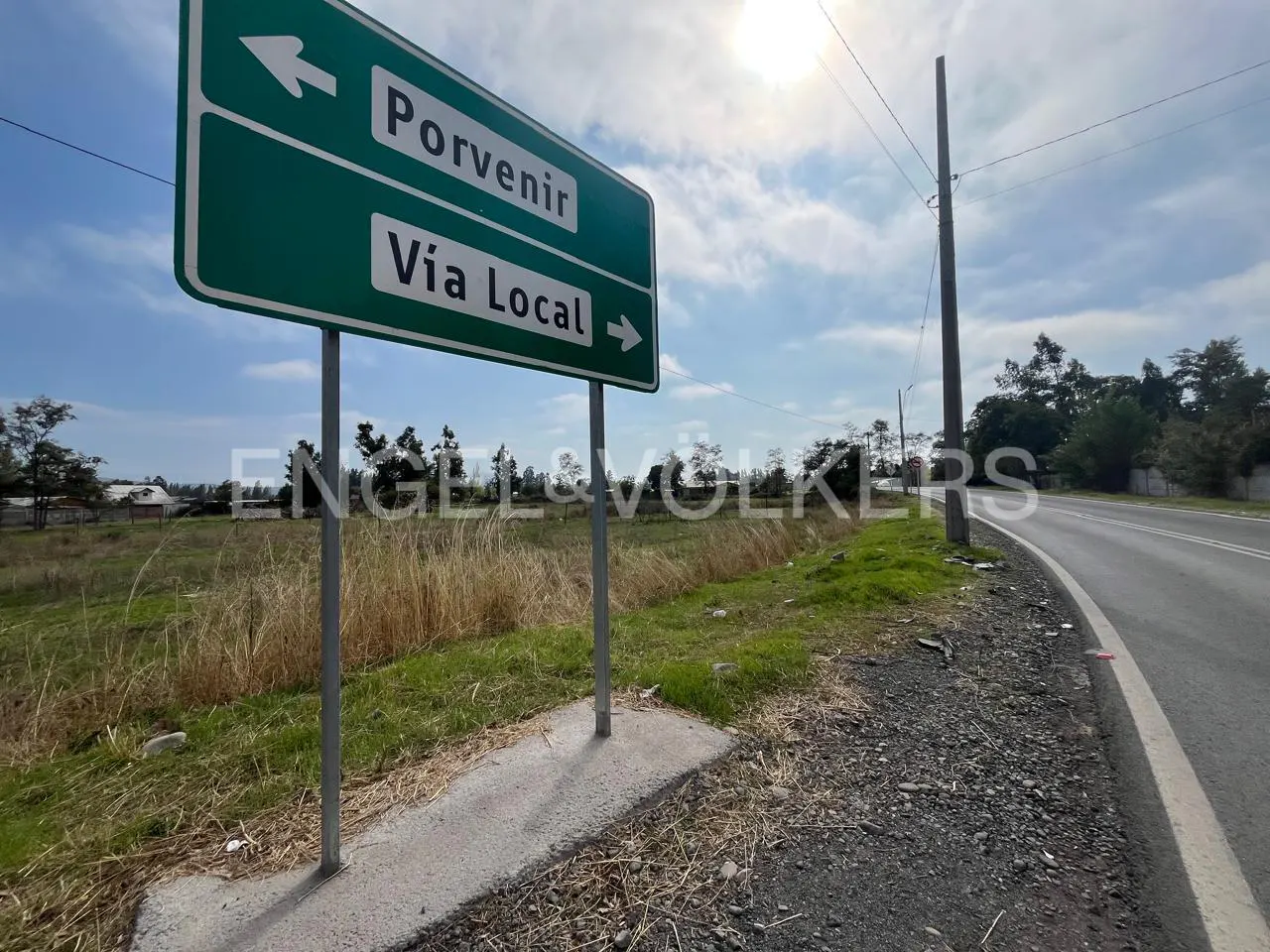 Green road sign reads "Porvenir" and "Via Local" with arrows. Vacant land and road visible under a cloudy sky.