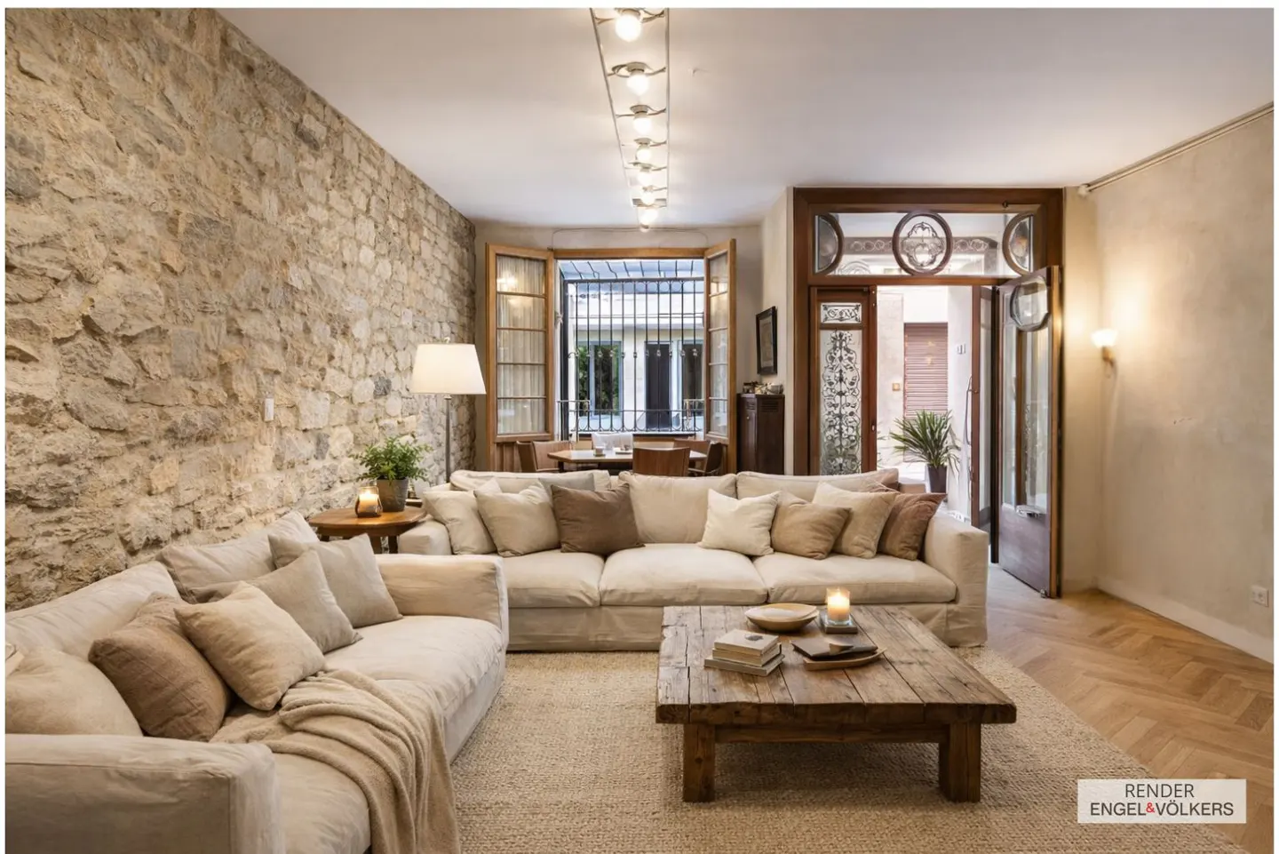 Living room with stone wall, beige sectional sofa, and rustic wood coffee table on a light rug. Open doors lead to an outdoor area.