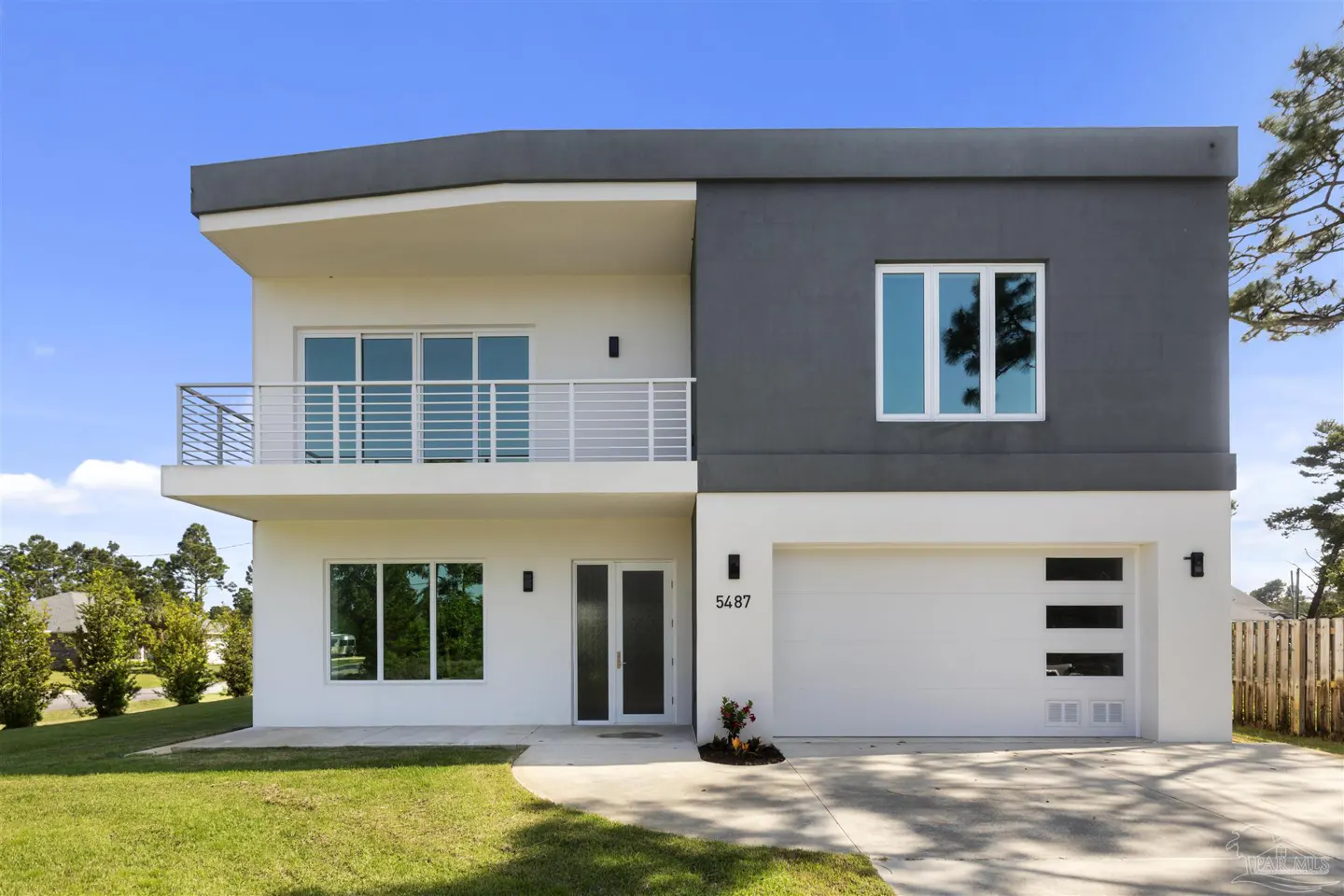 Two-story modern home with white and gray exterior, balcony, and white garage door with horizontal windows. Lawn in front.