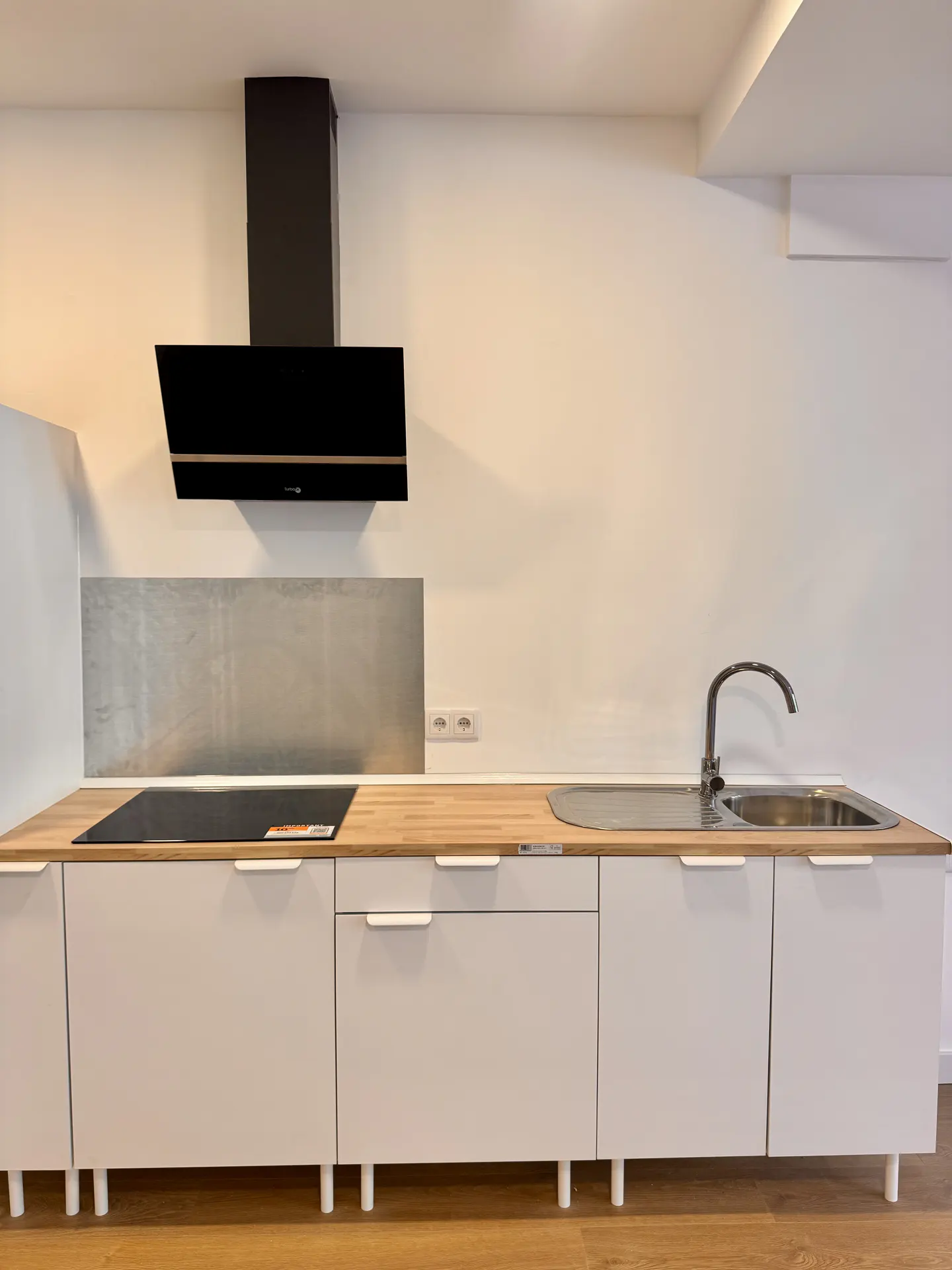 A modern kitchen with white cabinets, a wood countertop, and a stainless steel sink. A black range hood is mounted above the stove.