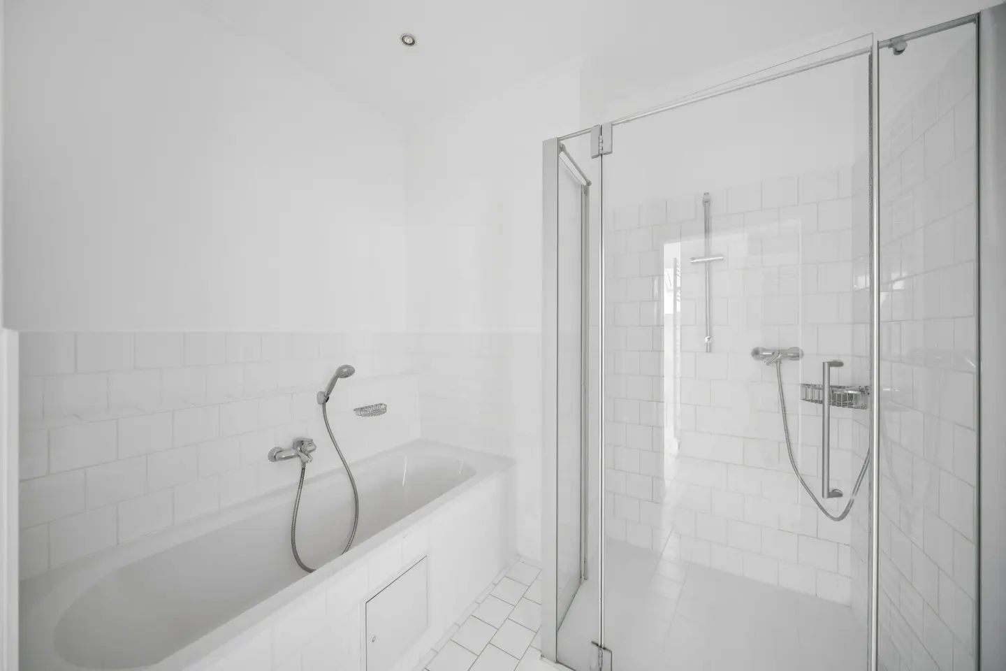 Bright, all-white bathroom with a bathtub and a glass-enclosed shower. White tile floor and walls. Bathtub has a shower head.