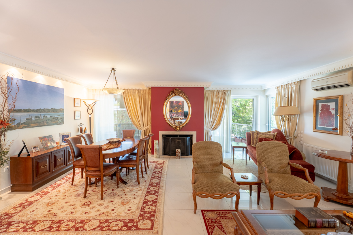 Spacious living and dining room with a red fireplace wall, ornate mirror, patterned rugs, and classic wooden furniture. [AI-generated text]