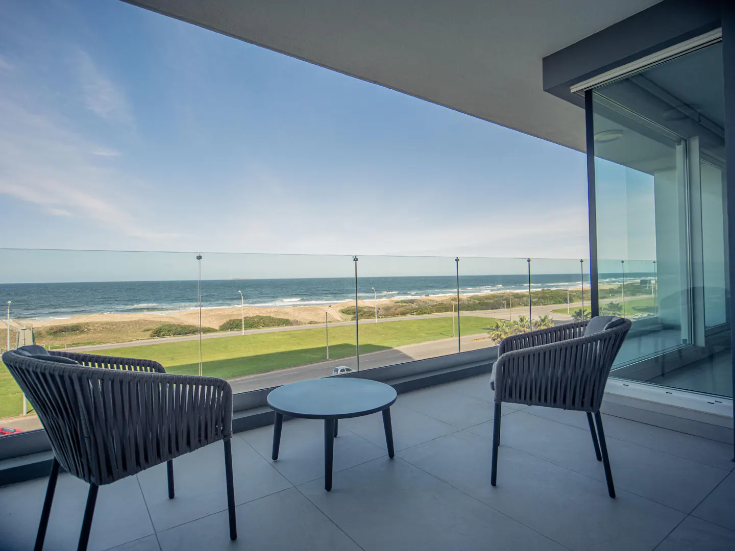 Balcony with two gray chairs and a small table overlooking the ocean on a sunny day.
