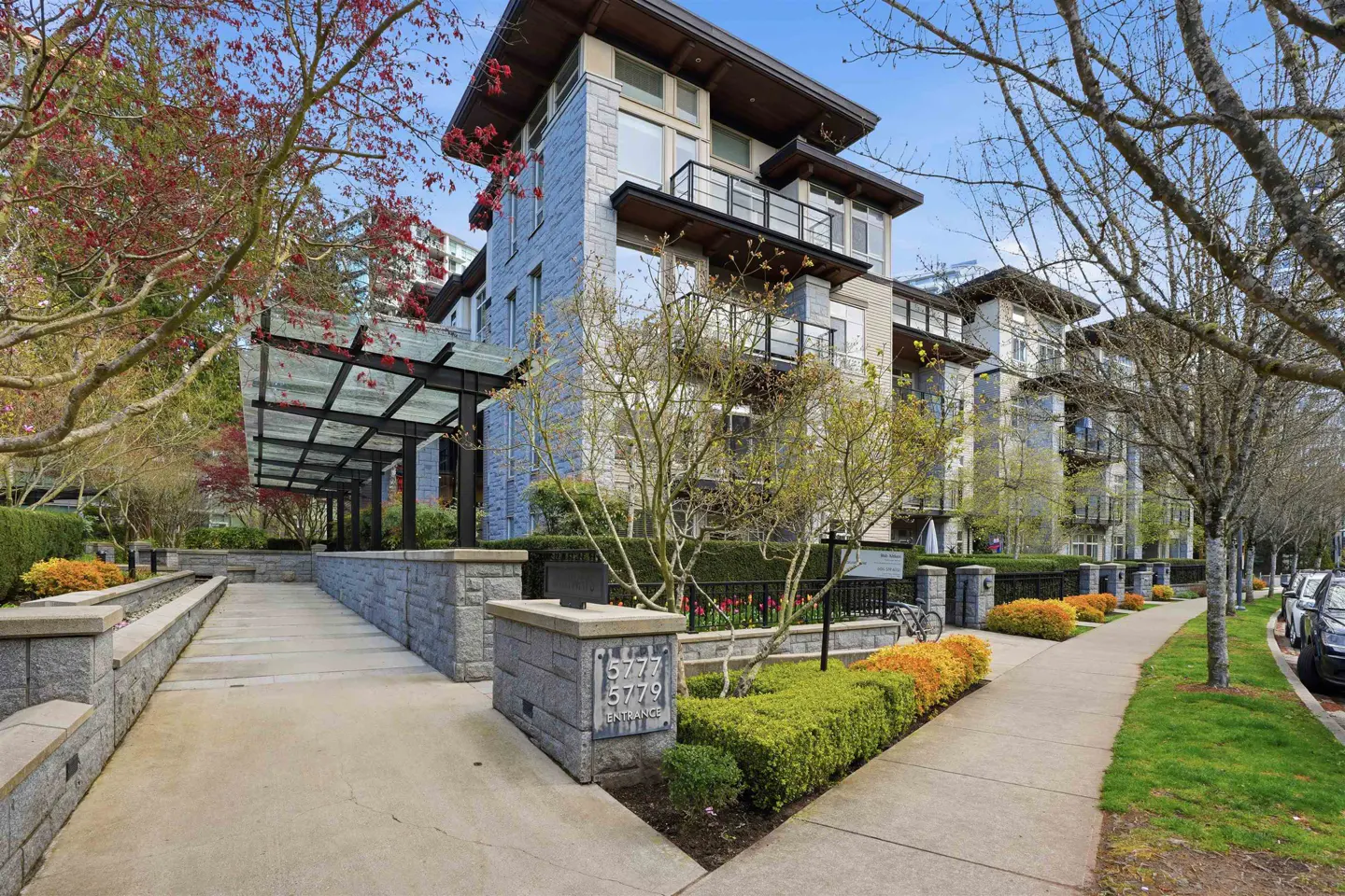 Exterior view of a modern, multi-story apartment building with stone facade, balconies, and landscaped grounds.