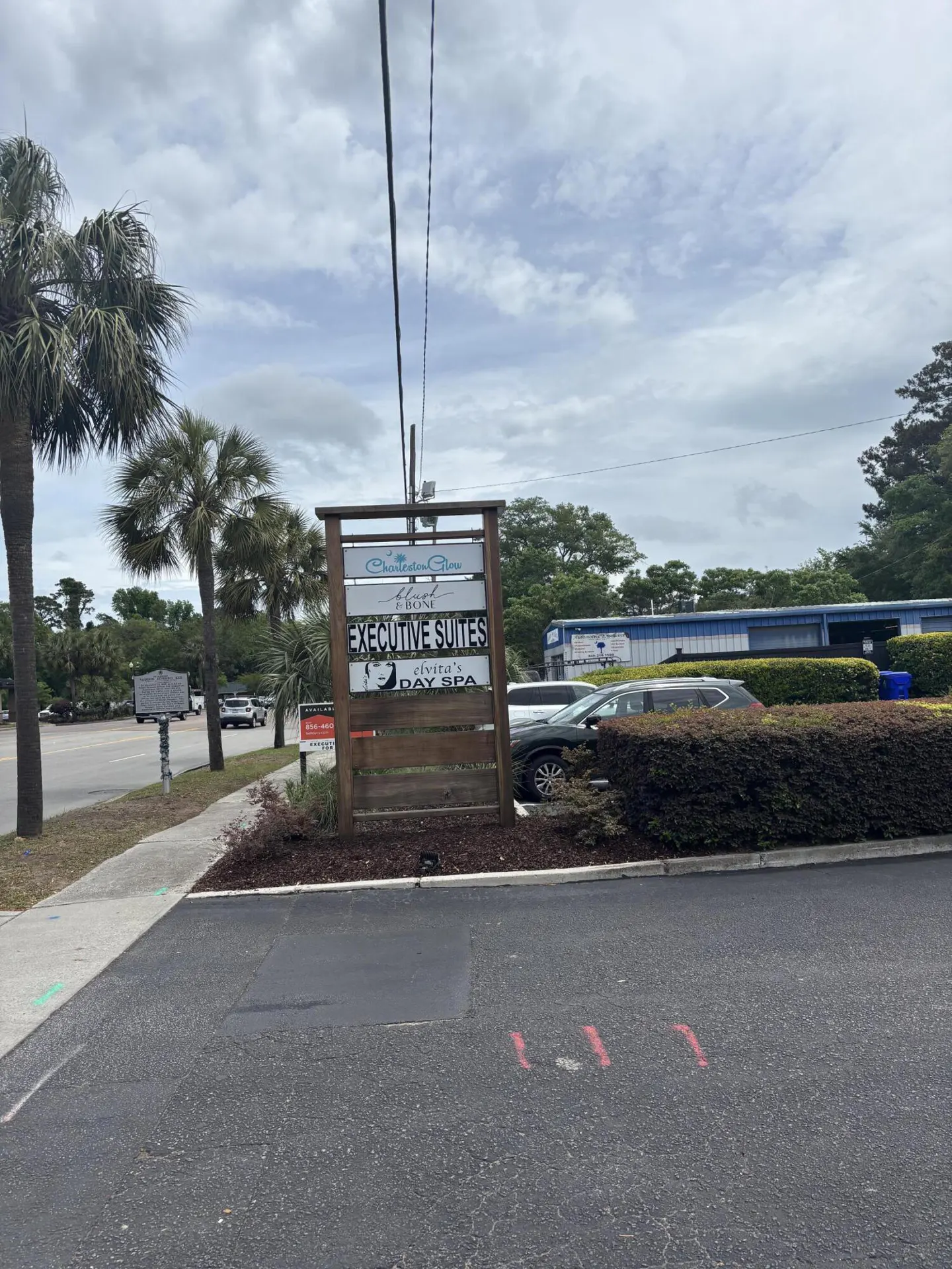 Outdoor sign for Charleston Glow Executive Suites and Elvita's Day Spa, with palm trees and cars in the background.