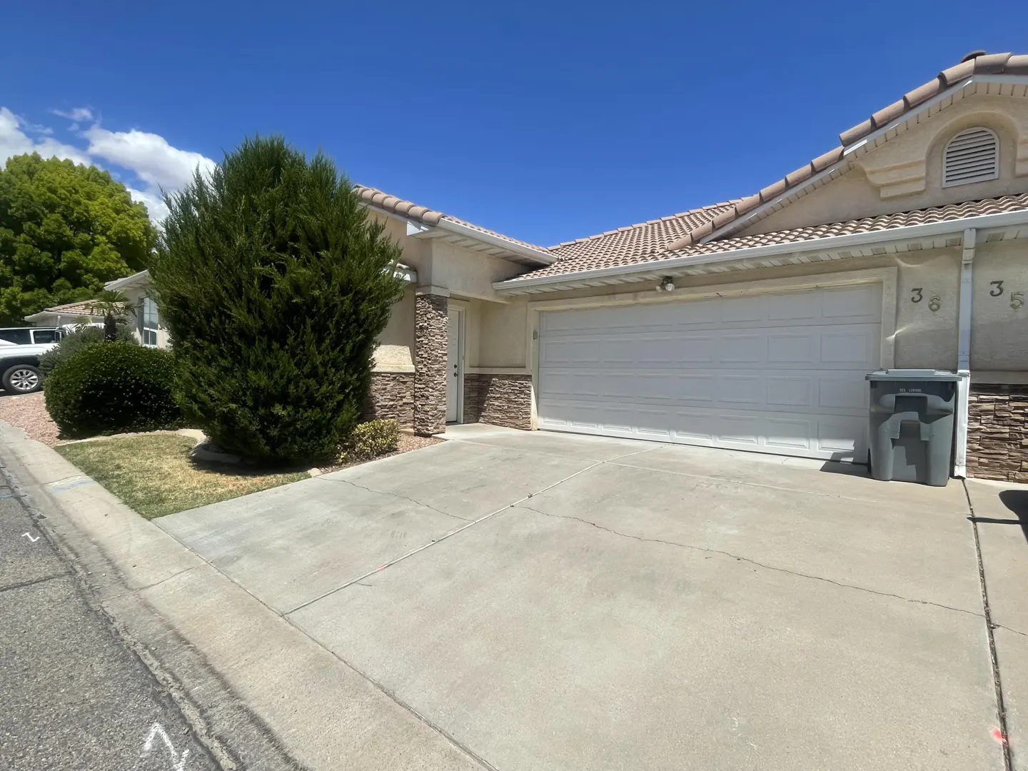 Beige single-story home with a white garage door, stone accents, and a concrete driveway under a blue sky.