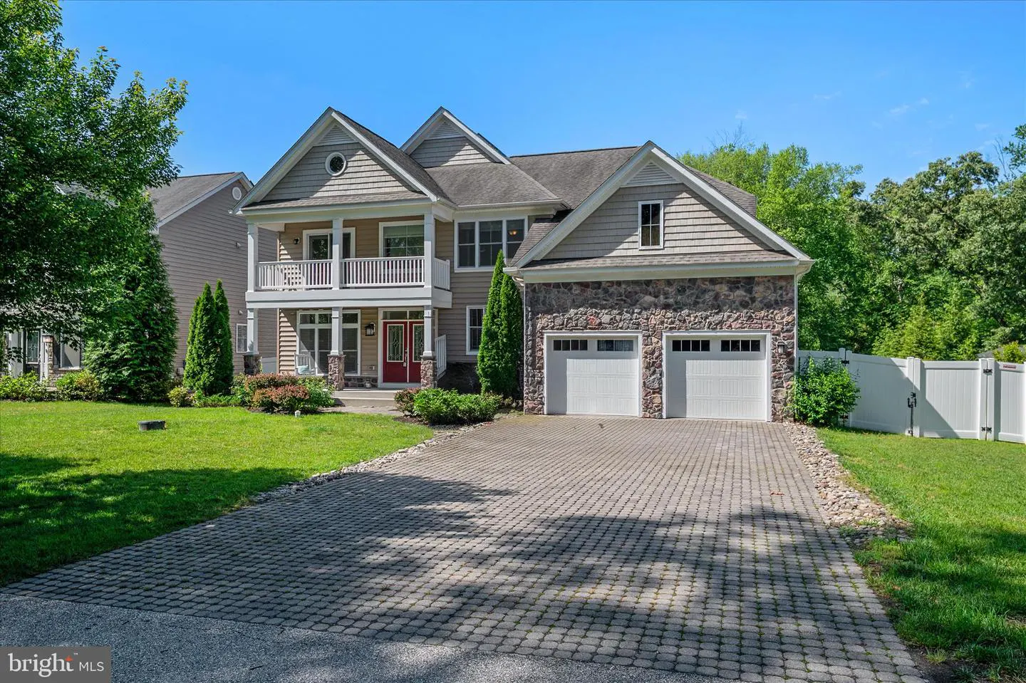 Two-story house with a stone garage, a red front door, and a brick driveway on a sunny day.