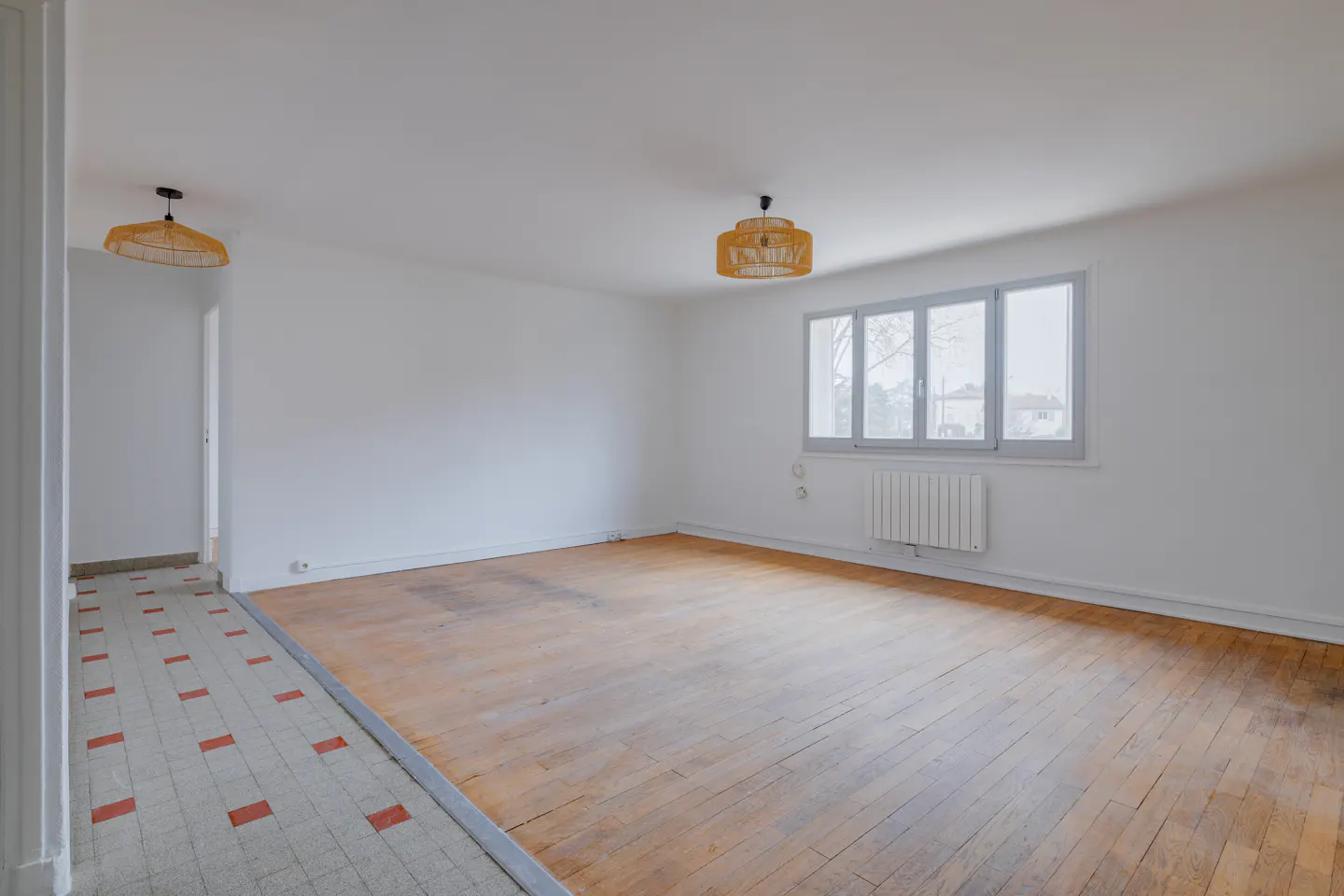 Bright, empty room with wood floors, white walls, and a window. Two straw light fixtures hang from the ceiling.