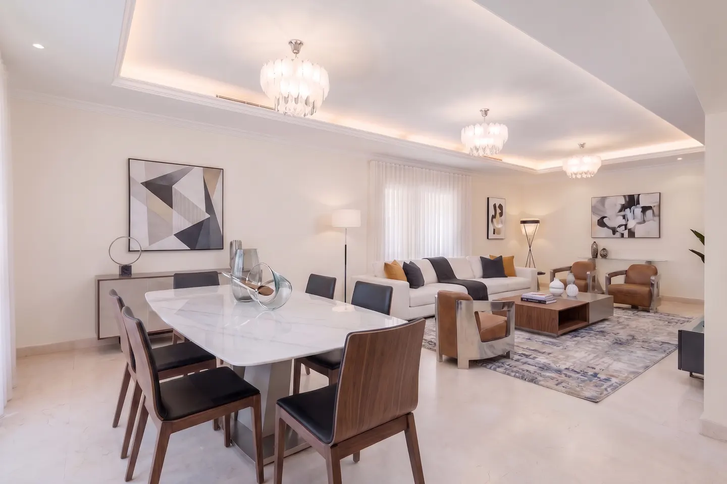Modern open-plan living and dining room with a white marble table, black chairs, white sofa, and tan leather armchairs.