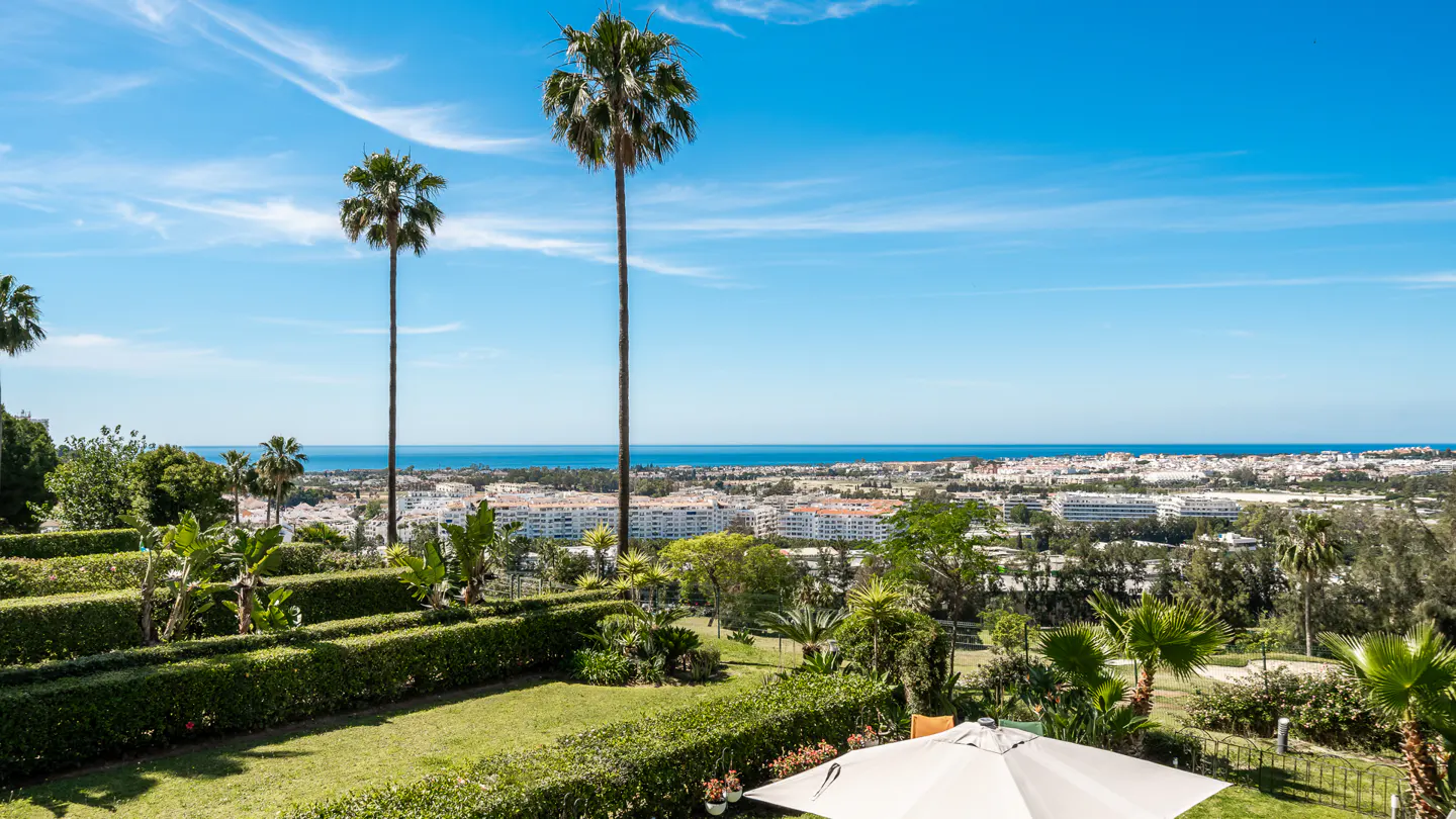 Scenic view of a coastal city with palm trees, green lawns, and a blue sky.