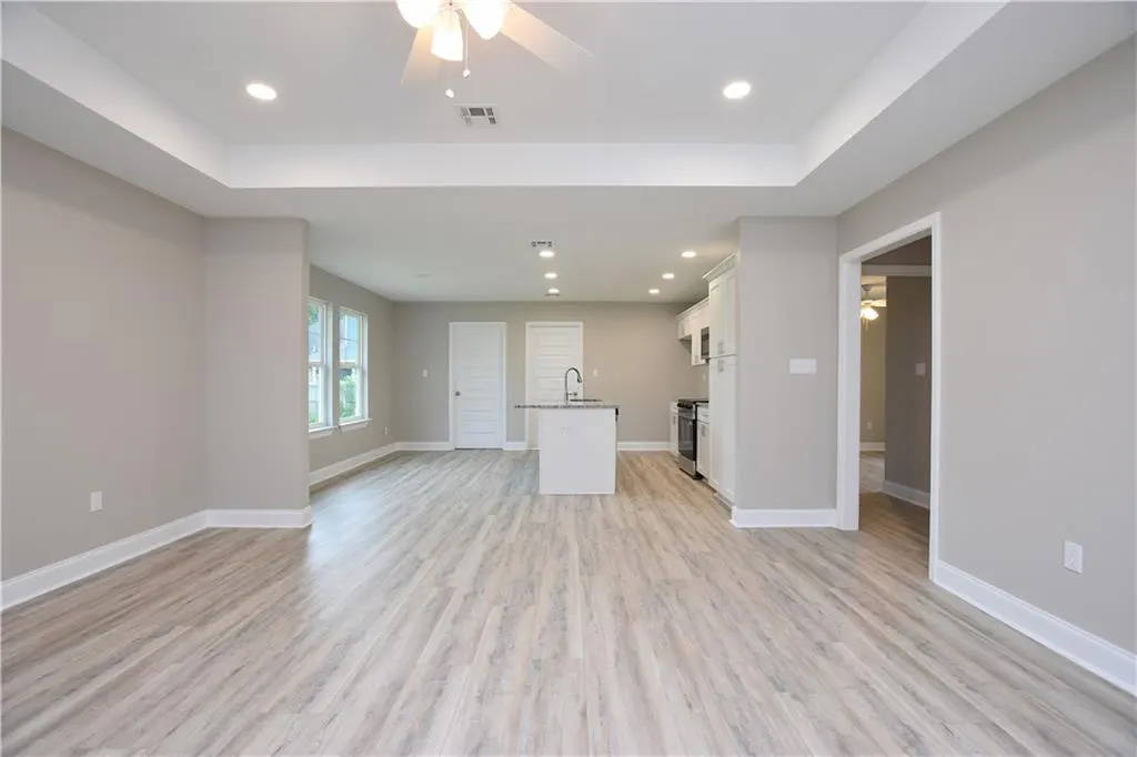 Open-concept living space with gray walls, light wood floors, and a white kitchen island. A ceiling fan and recessed lighting illuminate the room.