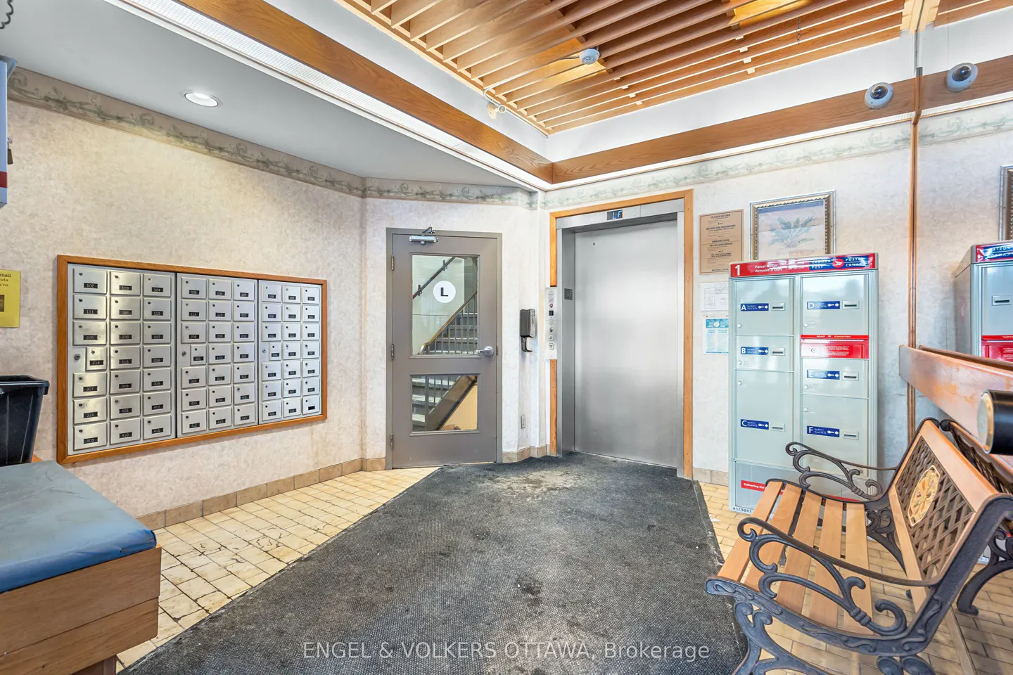 Interior view of a building lobby with mailboxes, elevator, bench, and stairs.