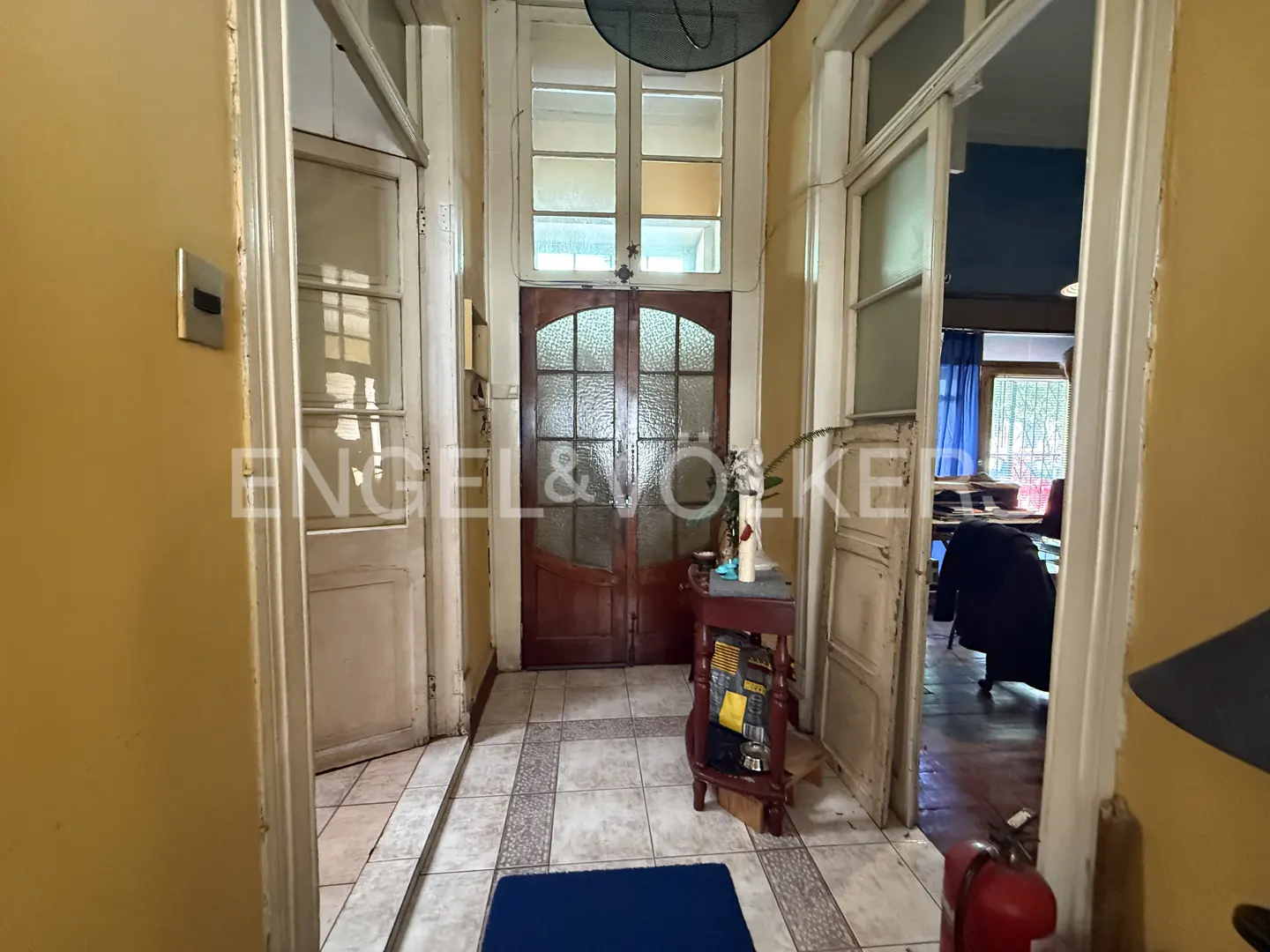 Foyer of a home with tiled floors, yellow walls, and white trim. A wooden door with glass panes is centered. A table with flowers sits to the right.
