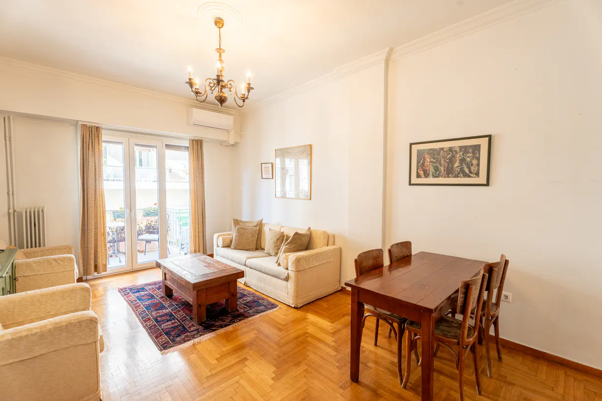 Living room with hardwood floors, a beige sofa, two armchairs, a wooden coffee table, and a dining table with four chairs.