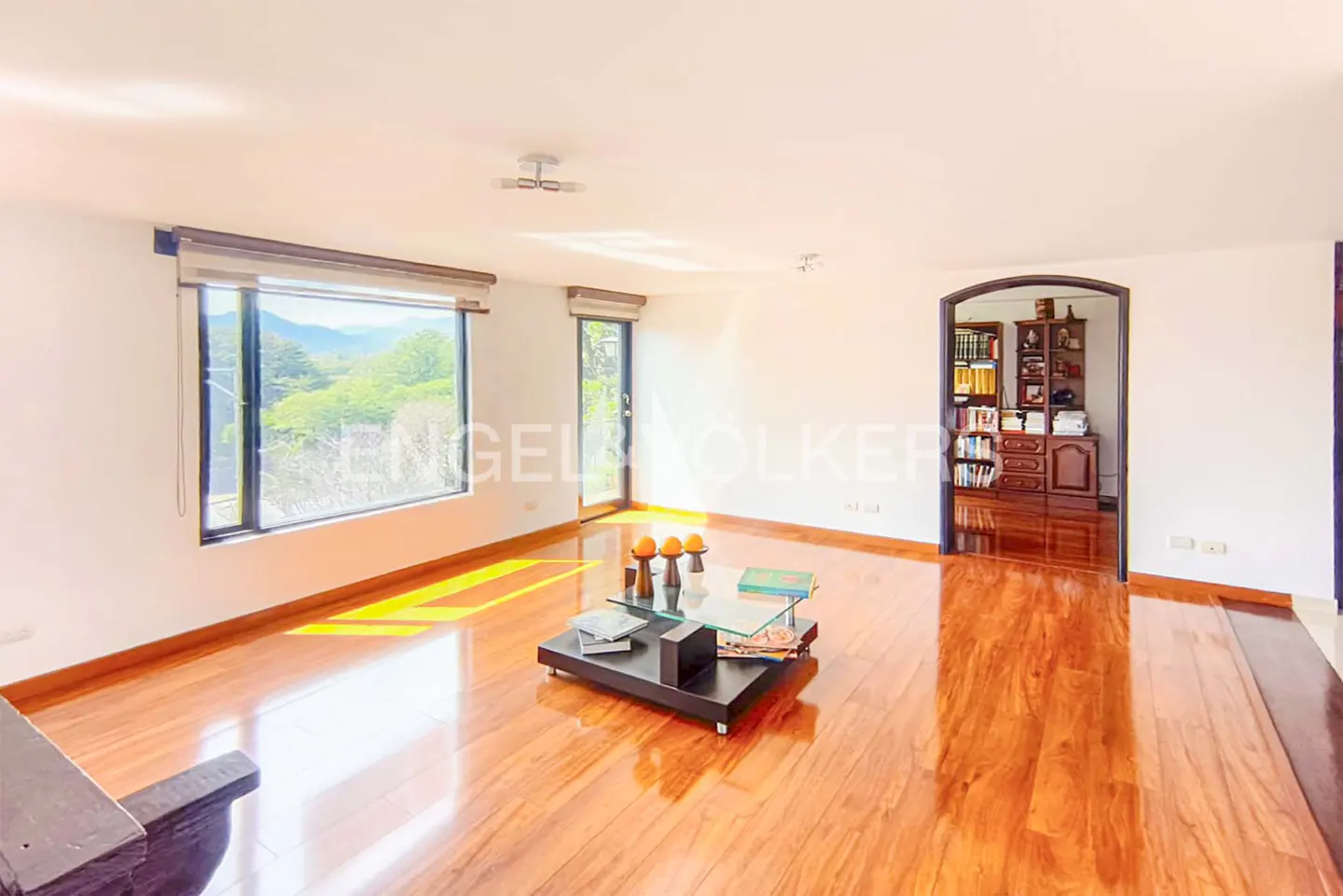 Bright living room with hardwood floors, a black coffee table, and a view of green hills through a large window.