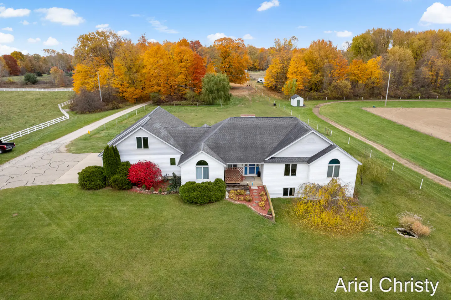 Aerial view of a white house with a gray roof, surrounded by green lawn and fall foliage.