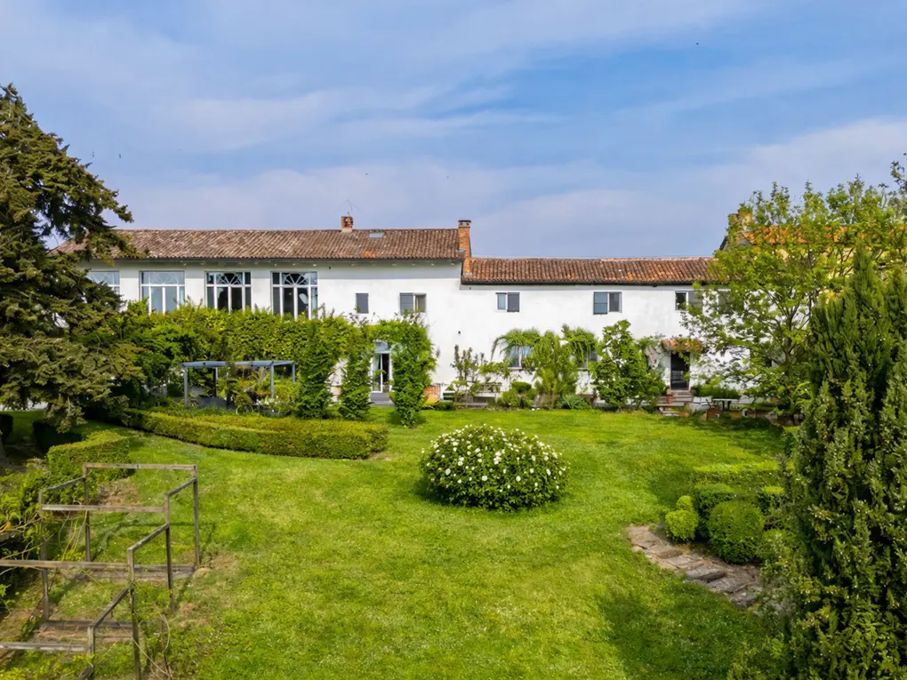 Exterior of a white, two-story house with a red tile roof and a green lawn with trees and bushes.