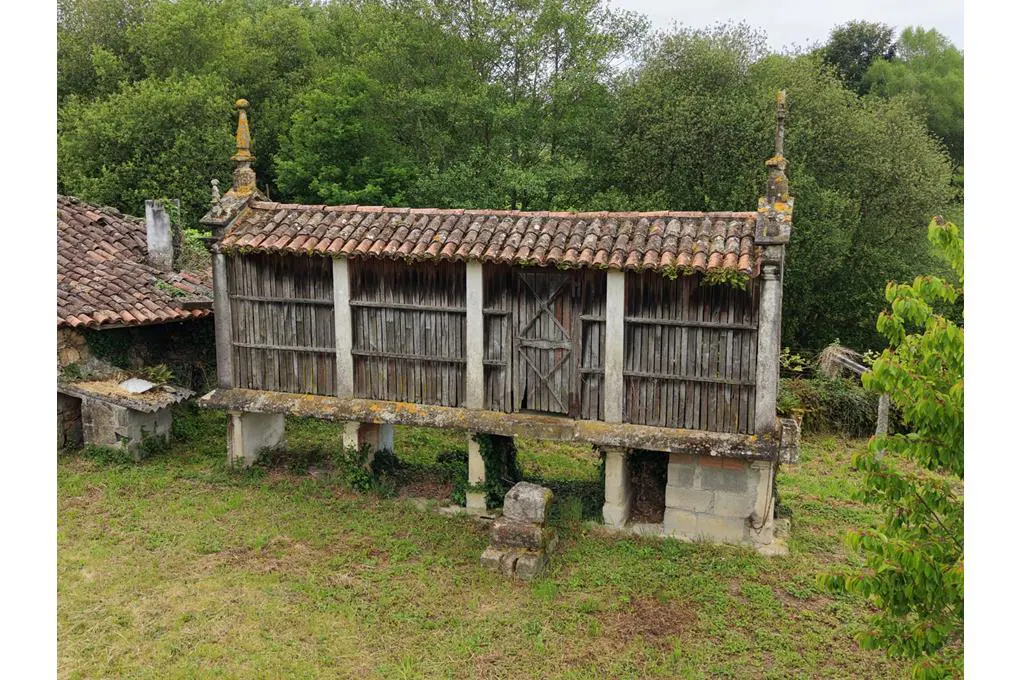 A traditional elevated wooden granary with a tiled roof, supported by stone pillars in a lush, green rural setting.