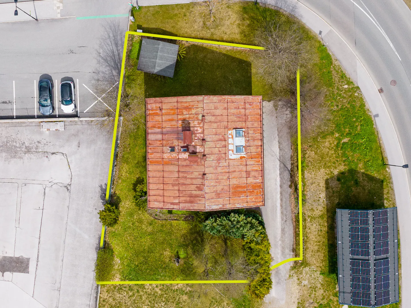 Aerial view of a property with a red-roofed building, outlined in yellow, next to a parking lot and solar panels.