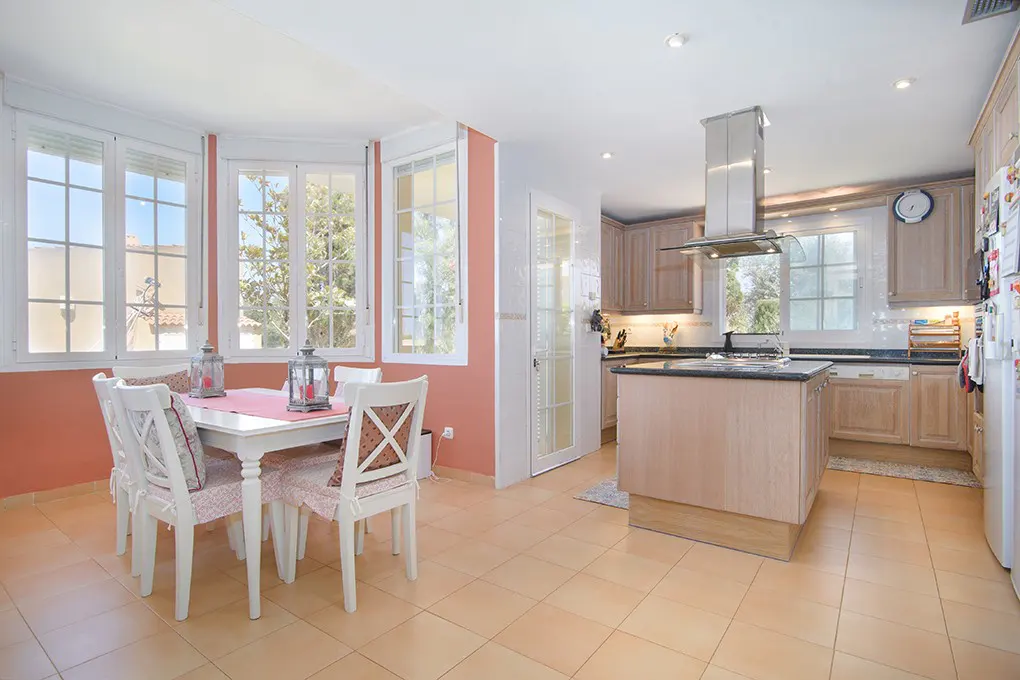 Bright kitchen with light wood cabinets, a central island, and a dining area with a white table against coral walls.
