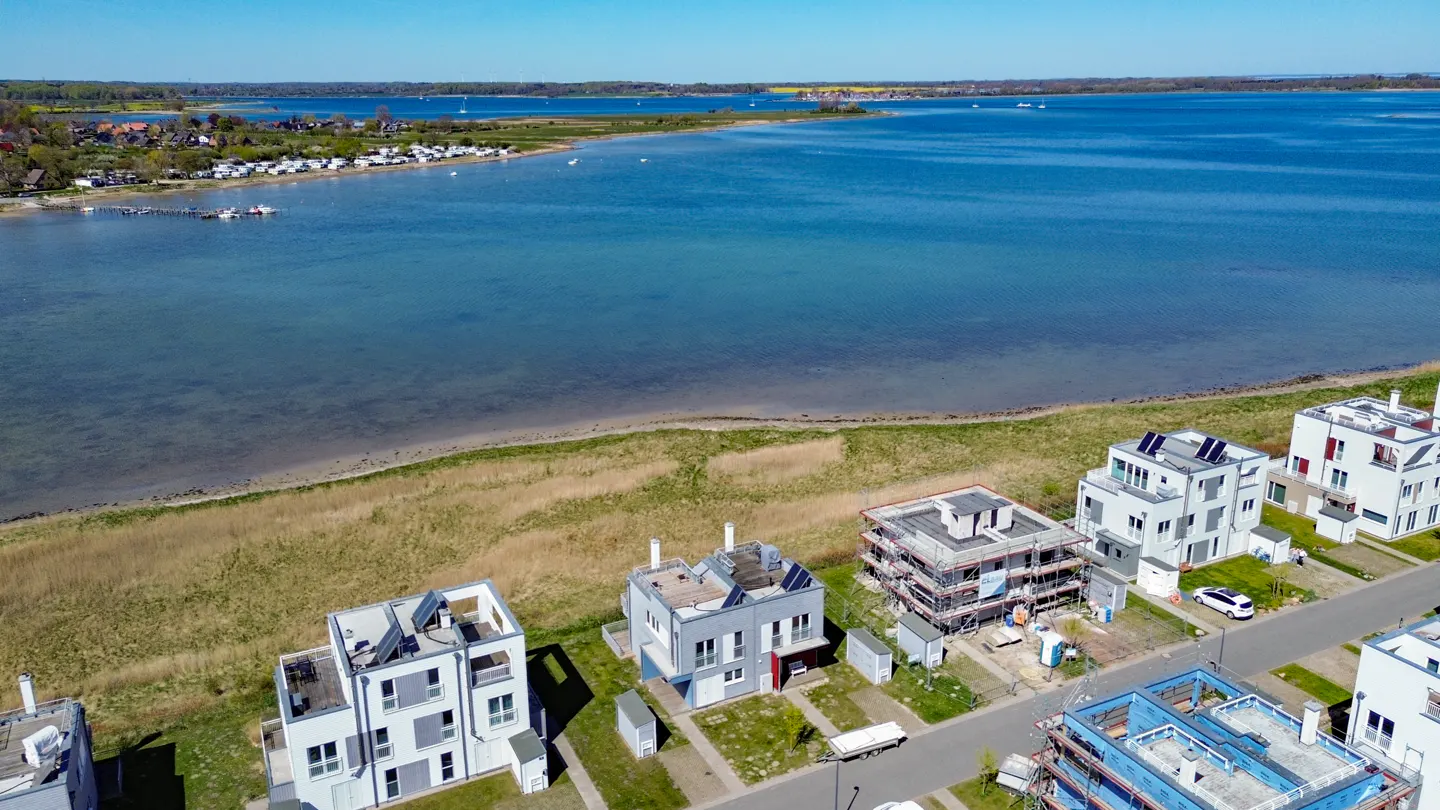 Aerial view of modern white houses near a blue bay, some under construction, on a sunny day.