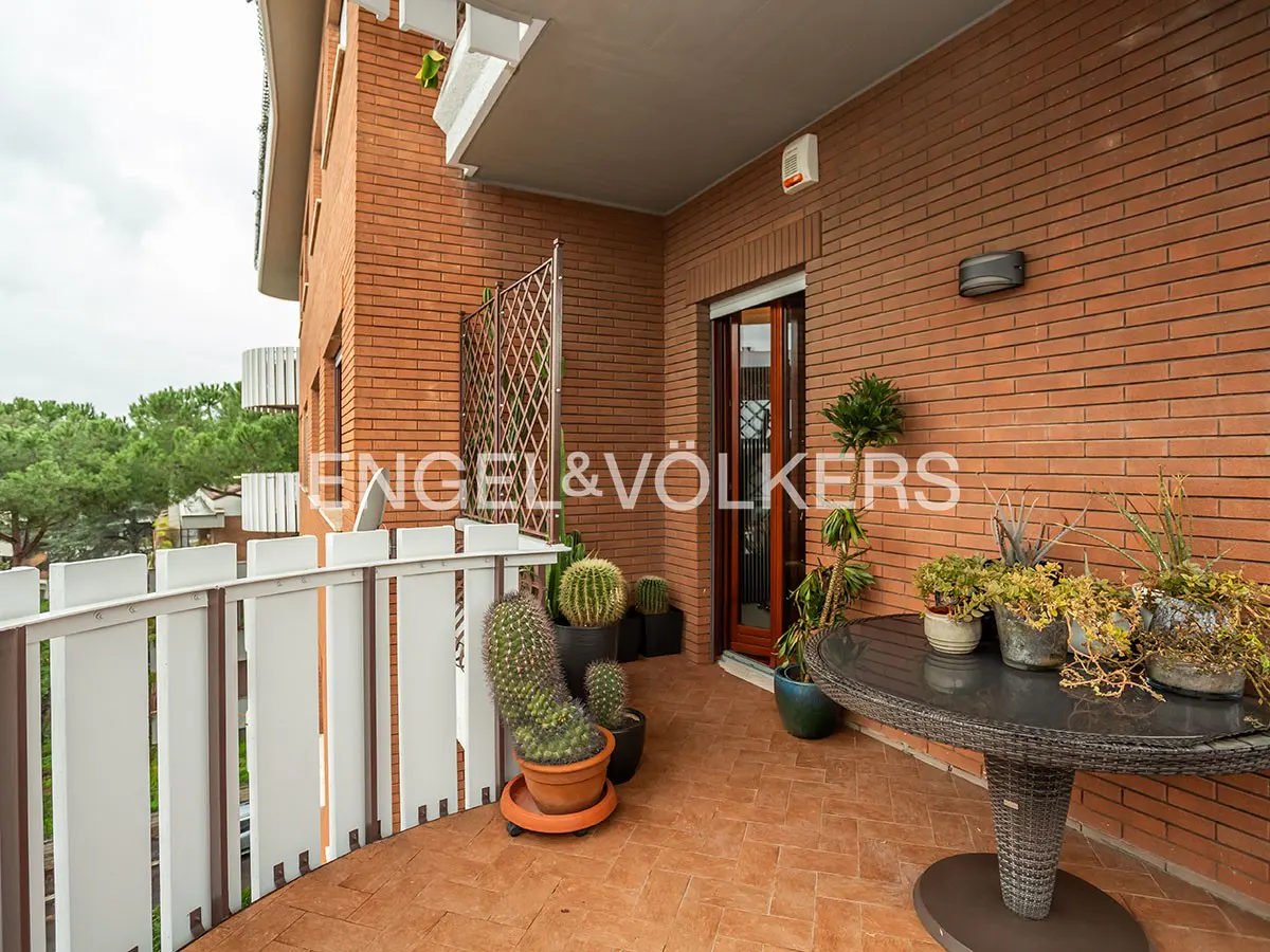 A brick balcony with potted plants, a round wicker table, and a white railing.