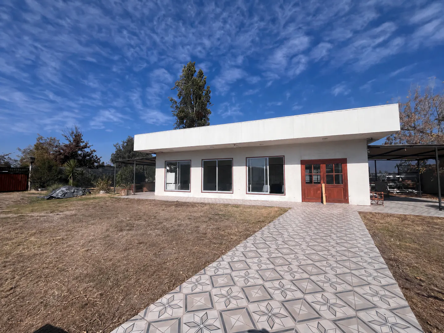 A modern white house with a patterned tile walkway, brown doors, and large windows under a blue sky.