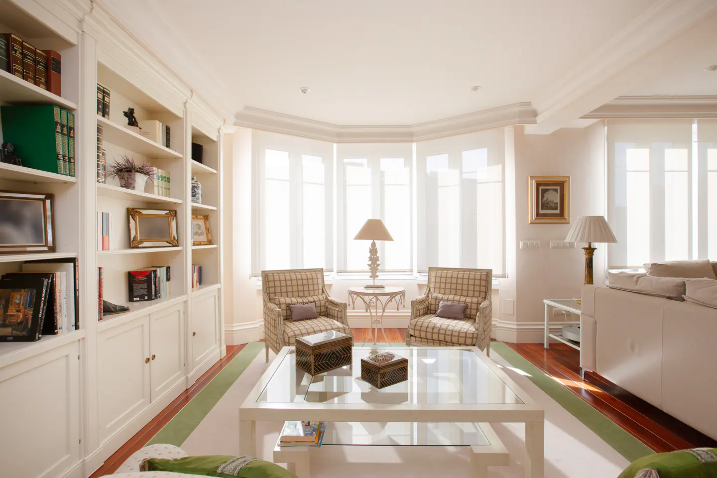 Bright living room with white built-in shelves, two plaid armchairs, and a glass coffee table on a green-striped rug.