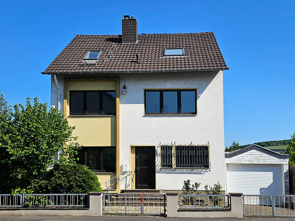 Two-story house with white and yellow facade, brown tiled roof, black door and windows, and a gray metal fence.