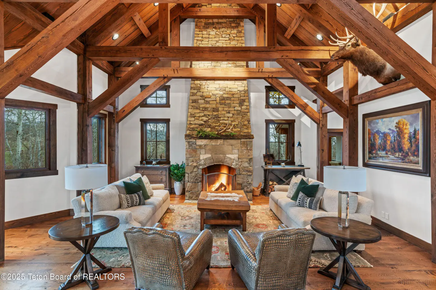 Rustic living room with vaulted timber ceilings, a stone fireplace, two sofas, leather armchairs, and an elk mount.