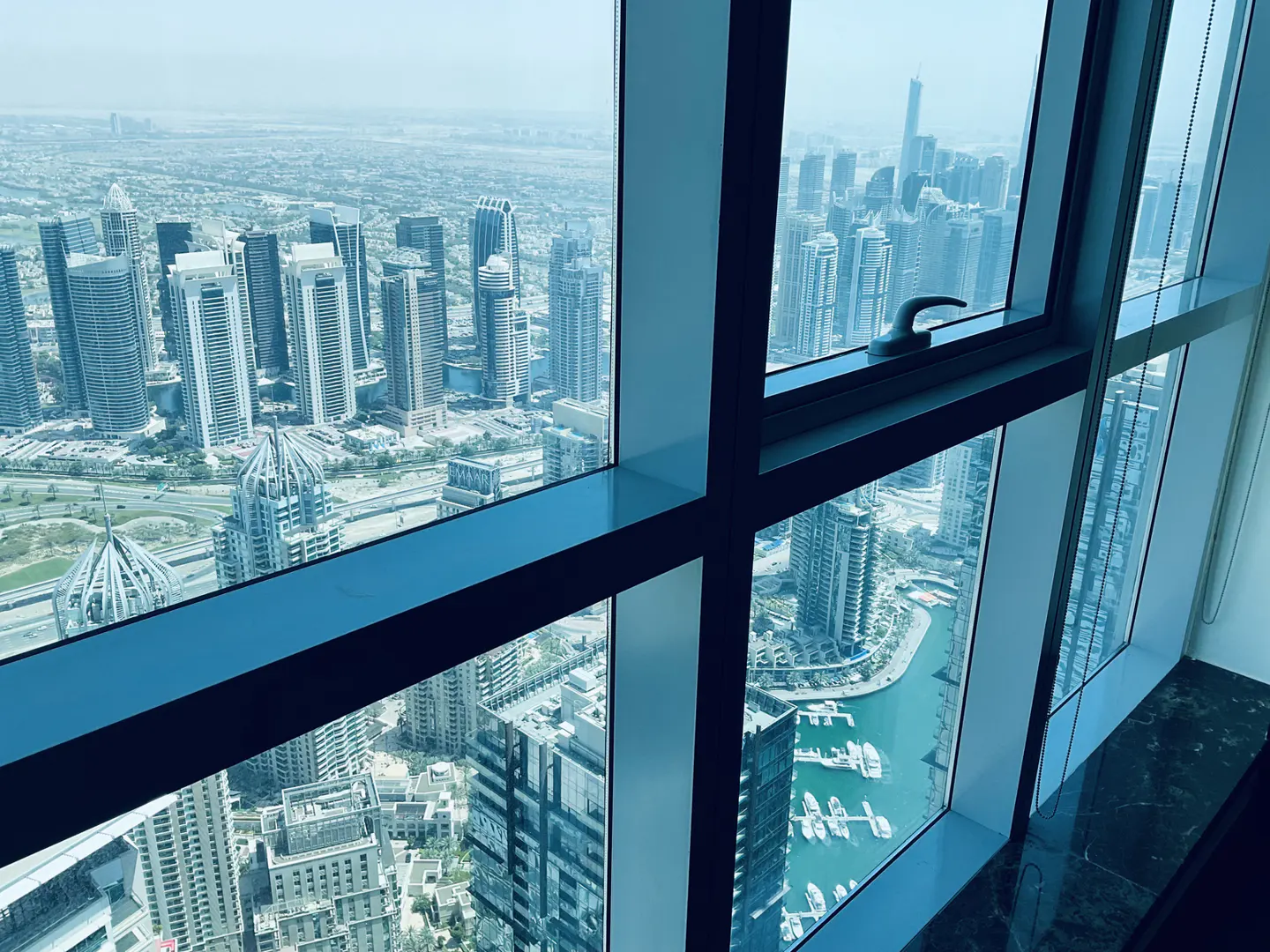 View from a high-rise window overlooking a city skyline with skyscrapers and a marina filled with boats.