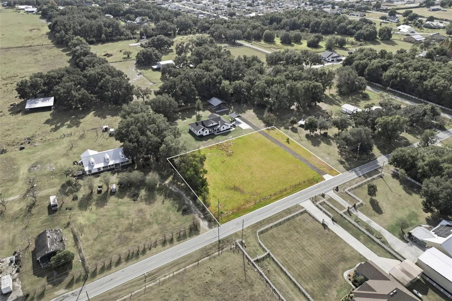 Aerial view of a rectangular vacant lot outlined in white, situated next to a road in a rural, tree-lined neighborhood.