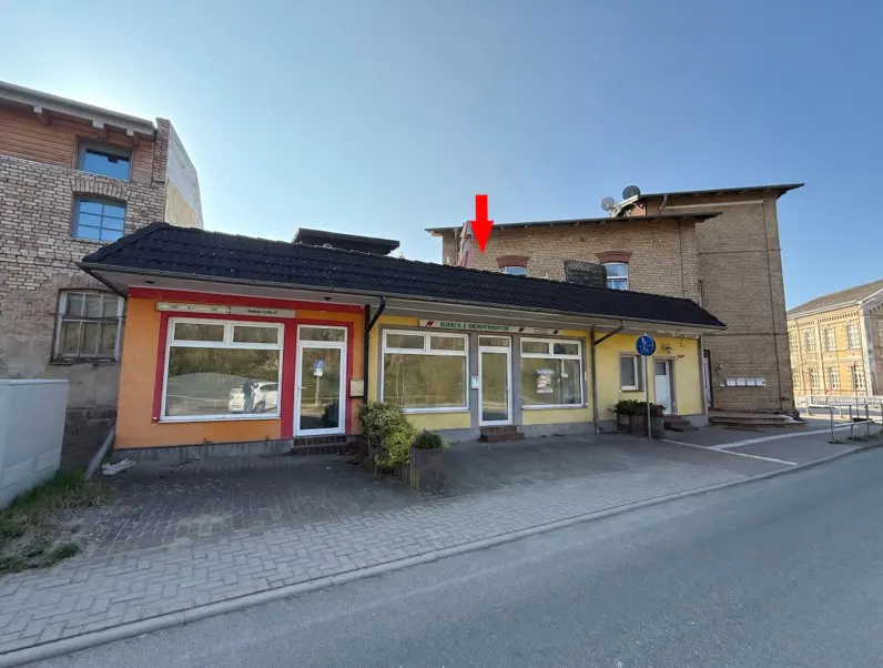 Exterior view of a one-story commercial building with orange and yellow facade, black roof, and large windows. A red arrow points to the building.